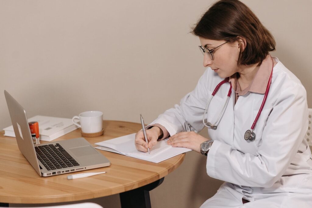 A doctor writing notes beside her laptop
