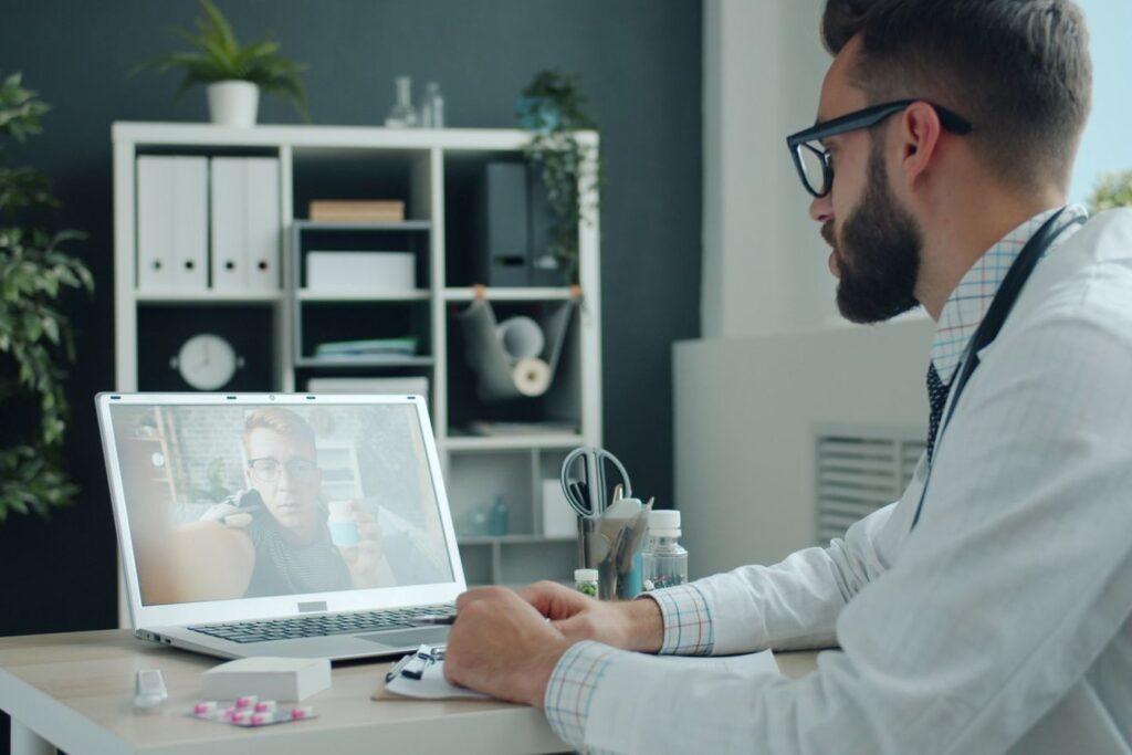 A doctor at his desk speaking with a patient on a video call