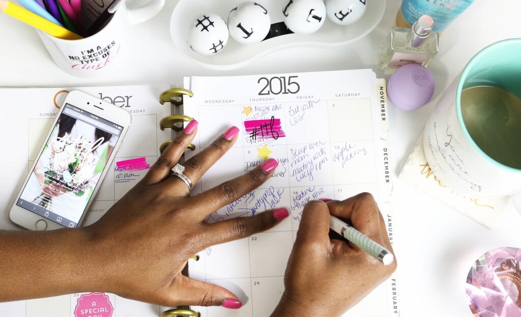 Hands writing entries into a paper planning calendar on a desk
